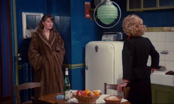 Movie still from “A Room in Town” (1982), directed by Jacques Demy – Two women standing at a table with a bottle of wine; Medium shot, Over the shoulder angle