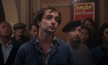 Movie still from “A Room in Town” (1982), directed by Jacques Demy – A group of men standing in front of each other in a room; Close Up shot, Over the shoulder angle