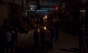 Movie still from “A Room in Town” (1982), directed by Jacques Demy – A group of people standing around in the dark; Extreme Wide shot, High angle