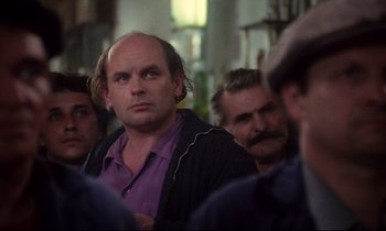 Movie still from “A Room in Town” (1982), directed by Jacques Demy – A group of men standing next to each other in a room; Medium shot, Over the shoulder angle