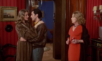 Movie still from “A Room in Town” (1982), directed by Jacques Demy – Two women and a man are standing in a living room; Medium shot, Over the shoulder angle