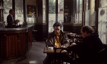 Movie still from “A Room in Town” (1982), directed by Jacques Demy – A man sitting at a table in a restaurant; Wide shot, Over the shoulder angle