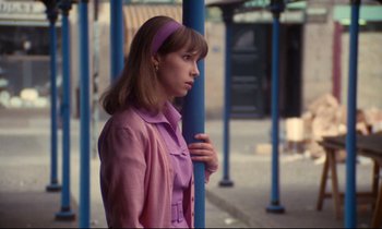 Movie still from “A Room in Town” (1982), directed by Jacques Demy – A woman in a pink jacket standing next to a blue pole; Medium shot, Low angle