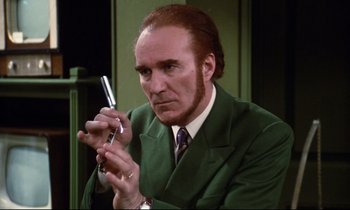 Movie still from “A Room in Town” (1982), directed by Jacques Demy – A man in a green suit holding a cell phone in his hand; Close Up shot, Low angle