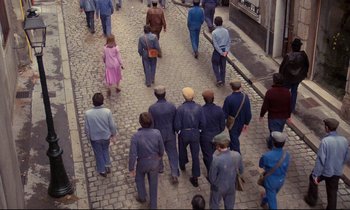 Movie still from “A Room in Town” (1982), directed by Jacques Demy – A group of people walking down a street; Wide shot, High angle