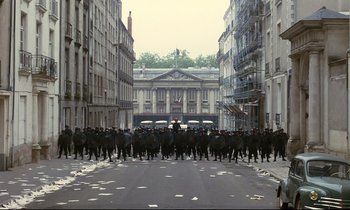 Movie still from “A Room in Town” (1982), directed by Jacques Demy – A group of people walking down a street; Extreme Wide shot, High angle