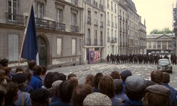 Movie still from “A Room in Town” (1982), directed by Jacques Demy – A crowd of people watching a parade of police officers; Extreme Wide shot, High angle