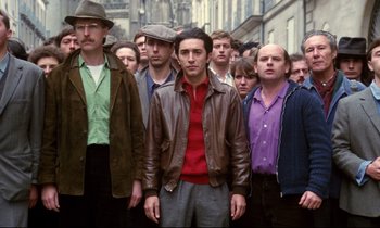 Movie still from “A Room in Town” (1982), directed by Jacques Demy – A group of men standing next to each other on a street; Medium shot, Low angle