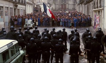 Movie still from “A Room in Town” (1982), directed by Jacques Demy – A group of people standing in front of a group of police officers; Extreme Wide shot, High angle