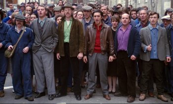 Movie still from “A Room in Town” (1982), directed by Jacques Demy – A group of men and women standing in a crowd; Wide shot, High angle