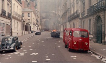 Movie still from “A Room in Town” (1982), directed by Jacques Demy – An old red fire truck is on fire in a city street; Extreme Wide shot, High angle