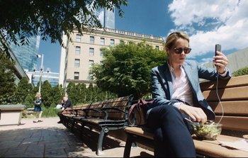 Movie still from “Unsane” (2018), directed by Steven Soderbergh – A woman sitting on top of a wooden park bench; Wide shot, Low angle