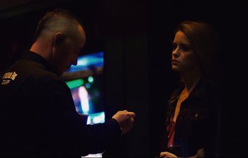 Movie still from “Unsane” (2018), directed by Steven Soderbergh – A man and a woman standing next to each other in a dark room; Medium shot, Over the shoulder angle