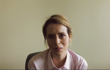 Movie still from “Unsane” (2018), directed by Steven Soderbergh – A woman sitting in a chair wearing a pink dress shirt; Close Up shot, Low angle