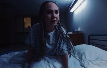 Movie still from “Unsane” (2018), directed by Steven Soderbergh – A woman sitting on top of a bed with dreadlocks; Close Up shot, High angle