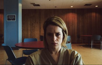 Movie still from “Unsane” (2018), directed by Steven Soderbergh – A woman in a tan robe sitting in front of a wooden wall; Close Up shot, Low angle