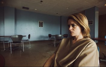 Movie still from “Unsane” (2018), directed by Steven Soderbergh – A woman sitting in front of a table in an empty room; Close Up shot, Low angle