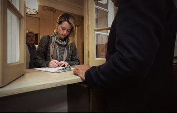 Movie still from “Unsane” (2018), directed by Steven Soderbergh – A woman writing on a piece of paper at a counter; Medium shot, Low angle