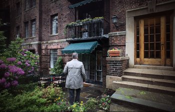 Movie still from “Unsane” (2018), directed by Steven Soderbergh – An older man standing in front of a brick building; Wide shot, Low angle