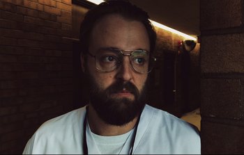 Movie still from “Unsane” (2018), directed by Steven Soderbergh – A man with a beard wearing glasses and a white shirt; Close Up shot, Low angle