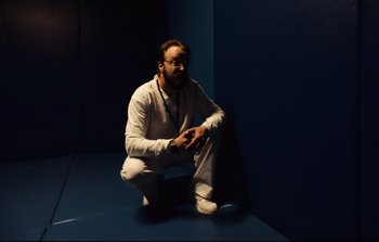Movie still from “Unsane” (2018), directed by Steven Soderbergh – A man crouching down in a room with a blue wall; Medium shot, Low angle