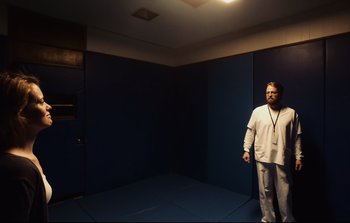 Movie still from “Unsane” (2018), directed by Steven Soderbergh – A man standing in a dark room with a light on; Wide shot, High angle