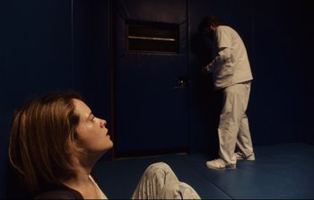 Movie still from “Unsane” (2018), directed by Steven Soderbergh – A woman sitting on the ground in front of a man; Wide shot, Low angle