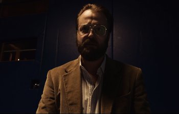 Movie still from “Unsane” (2018), directed by Steven Soderbergh – A man with a beard wearing a suit and glasses; Close Up shot, Low angle