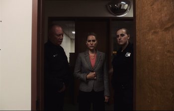 Movie still from “Unsane” (2018), directed by Steven Soderbergh – A woman standing between two police officers in a room; Medium shot, Over the shoulder angle