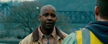 Movie still from “Unstoppable” (2010), directed by Tony Scott – A bald man with a brown jacket is standing in front of a bridge; Close Up shot, Over the shoulder angle