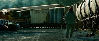 Movie still from “Unstoppable” (2010), directed by Tony Scott – A man standing in a parking lot next to train cars; Wide shot, Over the shoulder angle