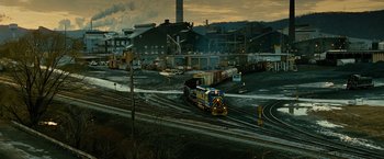 Movie still from “Unstoppable” (2010), directed by Tony Scott – A freight train traveling down tracks next to an industrial area; Extreme Wide shot, High angle