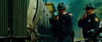 Movie still from “Unstoppable” (2010), directed by Tony Scott – A police officer holding up a cell phone to take a picture; Medium shot, Low angle