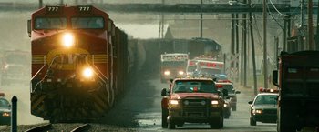 Movie still from “Unstoppable” (2010), directed by Tony Scott – A red truck driving down a street next to a train; Extreme Wide shot, Low angle