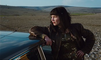 Movie still from “Until the End of the World” (1991), directed by Wim Wenders – A woman standing next to a car on the side of the road; Medium shot, Low angle
