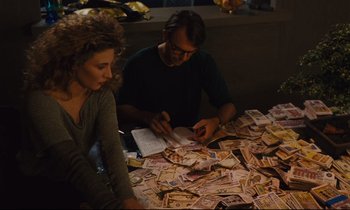 Movie still from “Until the End of the World” (1991), directed by Wim Wenders – A man and a woman sitting in front of a pile of money; Medium shot, High angle