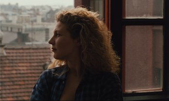 Movie still from “Until the End of the World” (1991), directed by Wim Wenders – A woman with long curly hair looking out of a window; Close Up shot, Low angle