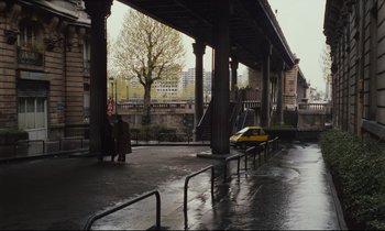 Movie still from “Until the End of the World” (1991), directed by Wim Wenders – A yellow taxi cab under an underpass on a rainy day; Extreme Wide shot, High angle