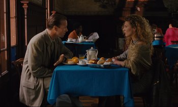 Movie still from “Until the End of the World” (1991), directed by Wim Wenders – A man and a woman sitting at a table with food; Medium shot, High angle