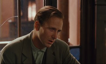 Movie still from “Until the End of the World” (1991), directed by Wim Wenders – A person wearing a suit and tie; Close Up shot, Over the shoulder angle
