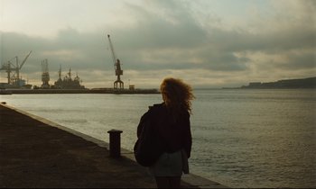 Movie still from “Until the End of the World” (1991), directed by Wim Wenders – A woman standing on the side of a pier looking out at the water; Extreme Wide shot, Low angle