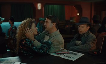 Movie still from “Until the End of the World” (1991), directed by Wim Wenders – A man and a woman sitting at a table with another man; Medium shot, Over the shoulder angle