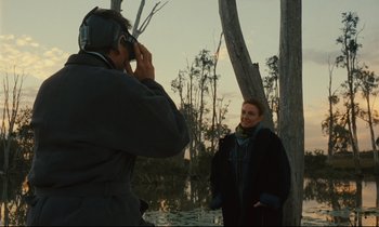 Movie still from “Until the End of the World” (1991), directed by Wim Wenders – A man taking a picture of a woman in a forest; Medium shot, Over the shoulder angle