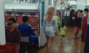Movie still from “Until the End of the World” (1991), directed by Wim Wenders – A group of people playing a slot machine game; Wide shot, Over the shoulder angle