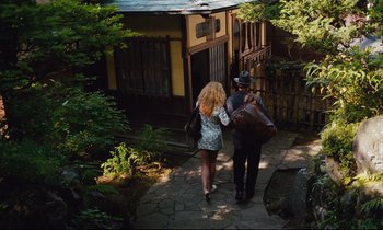Movie still from “Until the End of the World” (1991), directed by Wim Wenders – A man and a woman walking down a path in front of a house; Wide shot, High angle