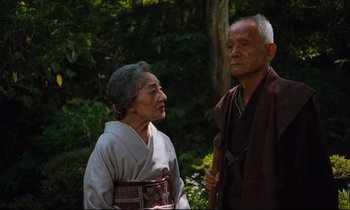Movie still from “Until the End of the World” (1991), directed by Wim Wenders – An older man standing next to an older woman; Medium shot, Low angle