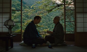 Movie still from “Until the End of the World” (1991), directed by Wim Wenders – Two men sitting in front of a window with trees in the background; Wide shot, Over the shoulder angle
