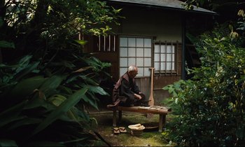 An old man sitting on a bench in front of a house