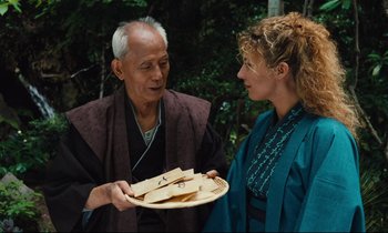 Movie still from “Until the End of the World” (1991), directed by Wim Wenders – An older man holding a plate of food and talking to a young woman; Medium shot, Over the shoulder angle