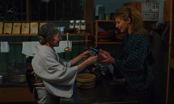Movie still from “Until the End of the World” (1991), directed by Wim Wenders – A woman is giving a woman a credit card in her hand; Medium shot, Low angle